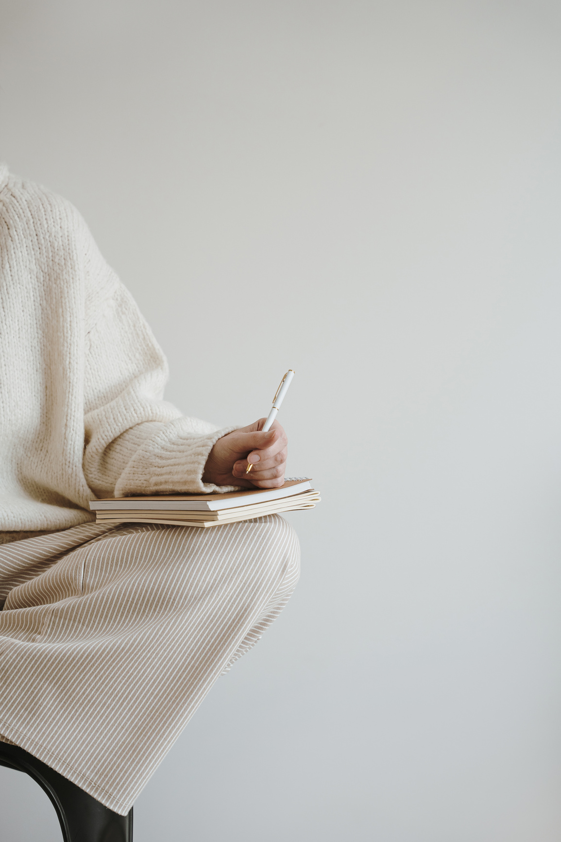 Someone in cream knitwear writing in a notebook
